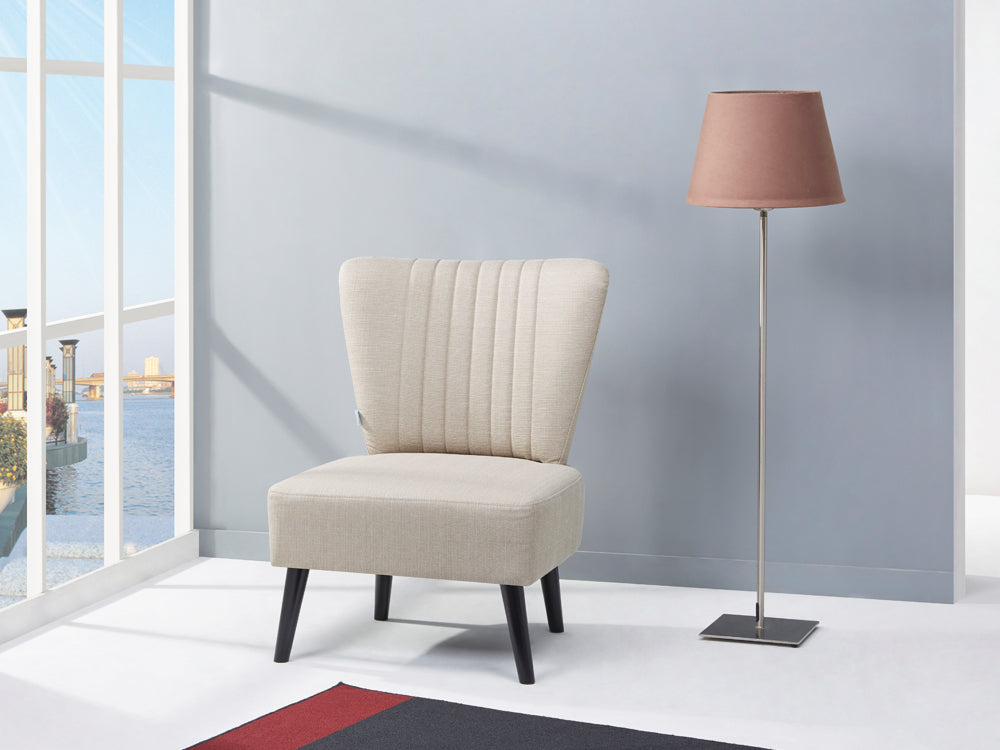 Anita Occasional Chair in cream fabric next to a modern brown lamp, set in a stylish room with large windows.