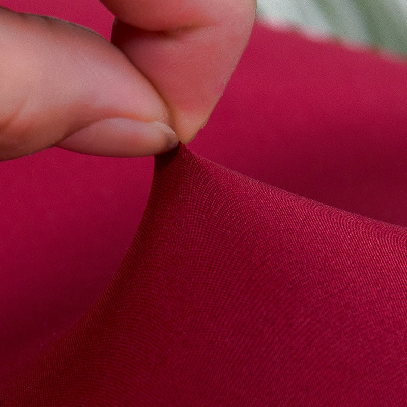 Close-up of a hand pulling the elastic fabric of a red couch cover, showcasing its stretch and quality.
